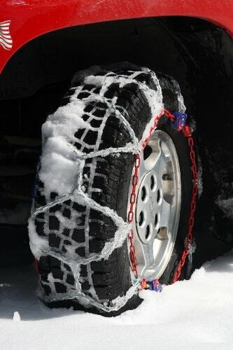 Car tire with snow chains on a snowy surface.